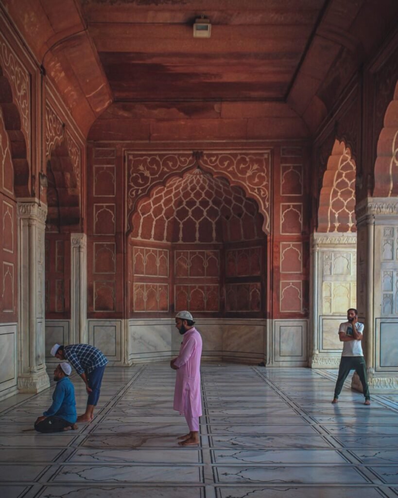 Muslim men praying inside a mosque with intricate arches and marble flooring, New Delhi.